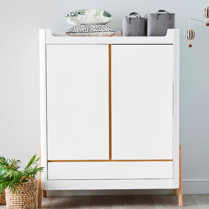 Gaia Baby Hera wardrobe in Scandi white and natural wood styled in a modern nursery, with storage baskets, indoor plants and decorative accessories displayed on top.