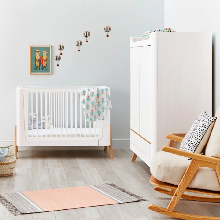 Modern nursery featuring the Gaia Baby Hera wardrobe in Scandi white and natural wood, styled alongside matching white baby cot, rocking chair and wall décor in a minimalist Scandinavian room