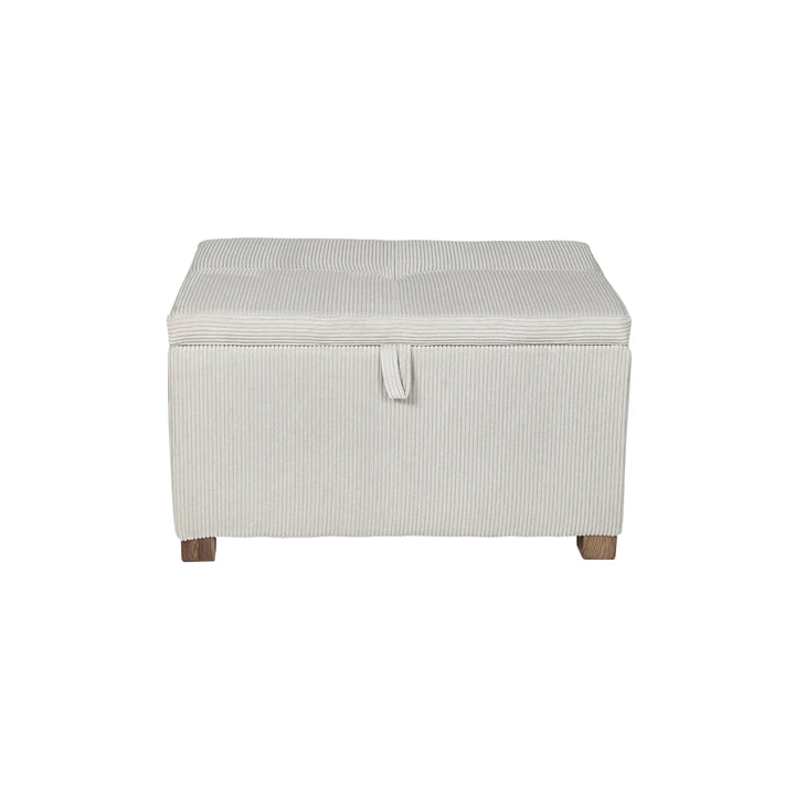 The Gaia Baby Serena Footstool in ecru corduroy fabric shown from the front on a white background, featuring a soft upholstered storage ottoman with textured corduroy finish, pull-tab lid detail, and dark wooden feet.