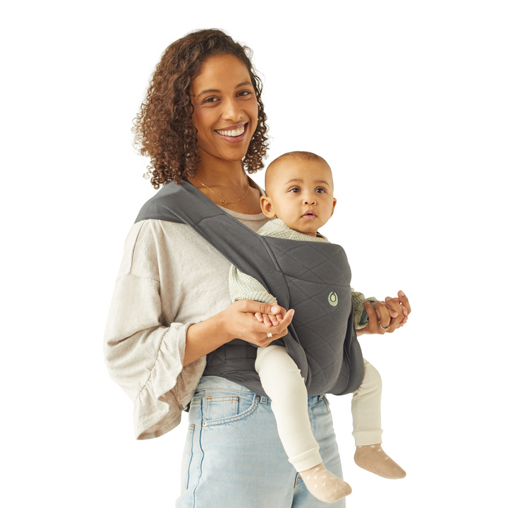 This image shows a smiling mum wearing her baby in the world facing position slightly angled to the right