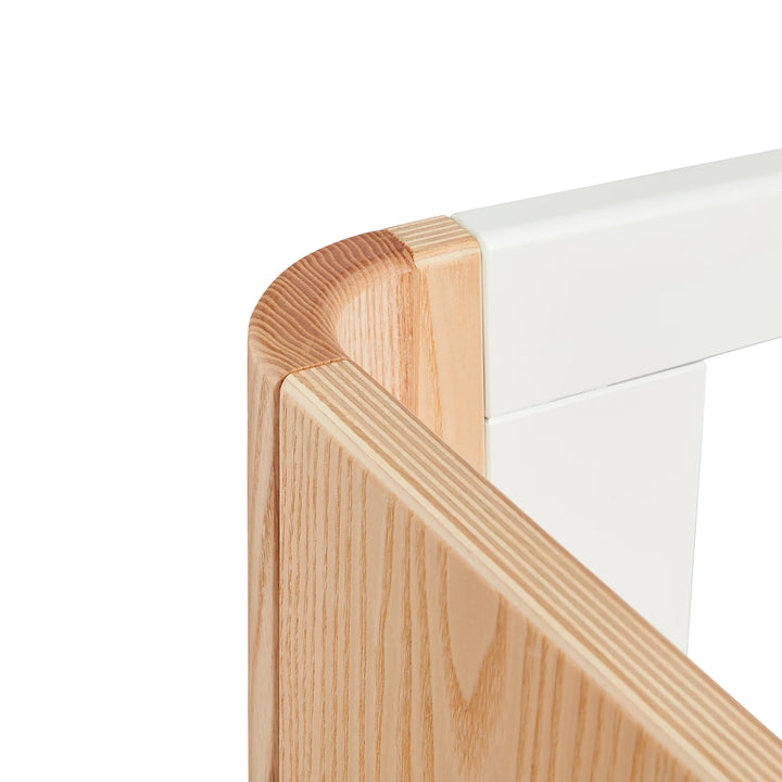 Close-up of Gaia Baby Hera cot in ash and walnut showing precision curved wood craftsmanship, smooth rounded corner detailing and premium Scandinavian sustainable nursery design.