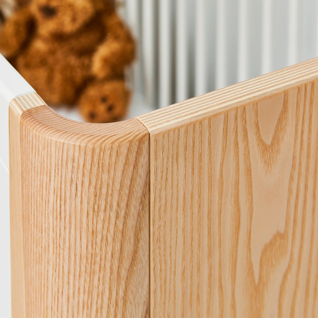 Close-up of Gaia Baby Hera cot in ash and walnut showing smooth curved solid wood corner detail with natural grain, highlighting premium Scandinavian craftsmanship in sustainable nursery furniture.