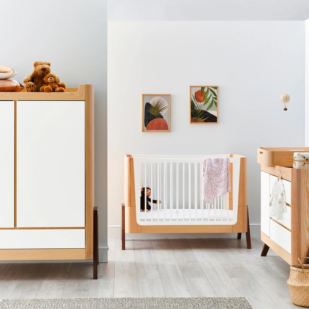 Beautiful Scandinavian nursery featuring the Gaia Baby Hera cot in ash and walnut with white slatted sides, matching dresser and wardrobe, natural wood accents, soft décor and toys — premium sustainable baby furniture for modern family homes.