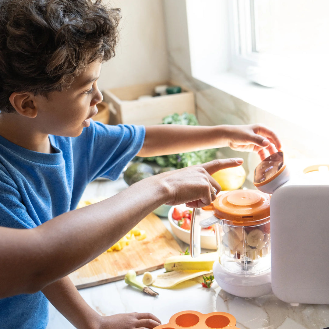Child helping to prepare healthy baby food using the Quook by Quark 5-in-1 baby food maker in kitchen.