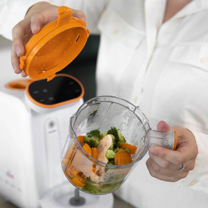 Parent using Quook by Quark 5-in-1 baby food maker to steam veg in transparent jug.