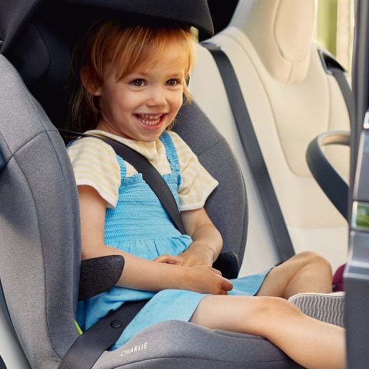 Child using the Swandoo Charlie armrest accessory while seated comfortably in a booster car seat inside a vehicle