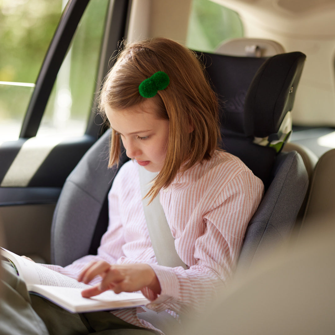 Child seated comfortably in the Swandoo Charlie i-Size booster seat while reading