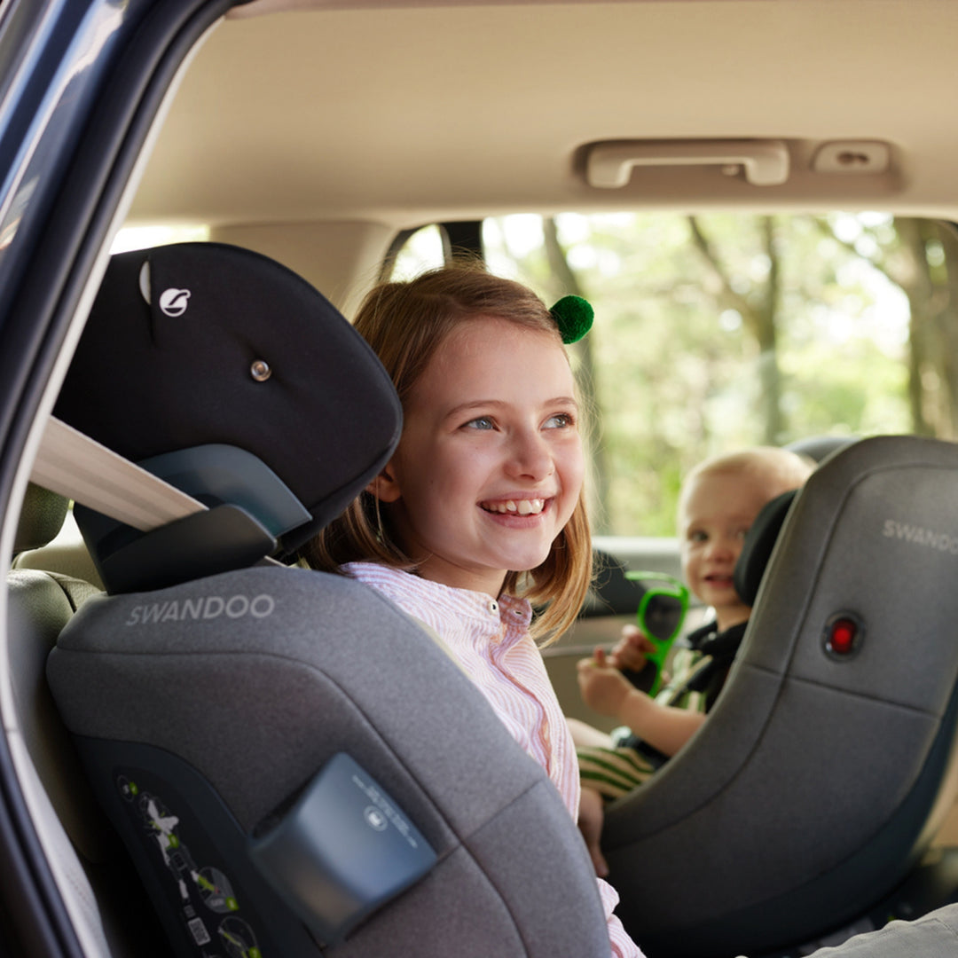Child seated in the Swandoo Charlie i-Size booster car seat with younger passenger beside her
