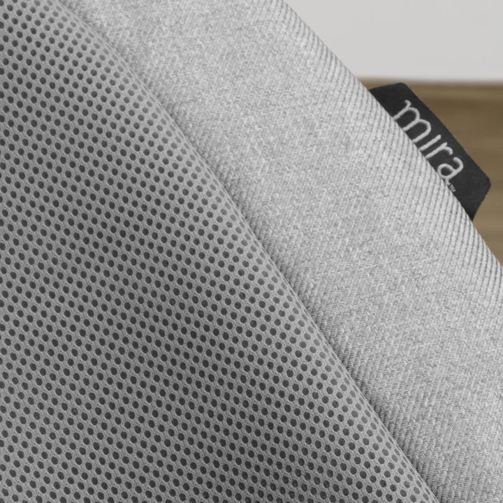 Close-up detail of the UPPAbaby Mira Bouncer in Stella grey, highlighting the breathable mesh seat fabric, soft textured upholstery, and branded Mira tag for premium baby comfort and airflow.