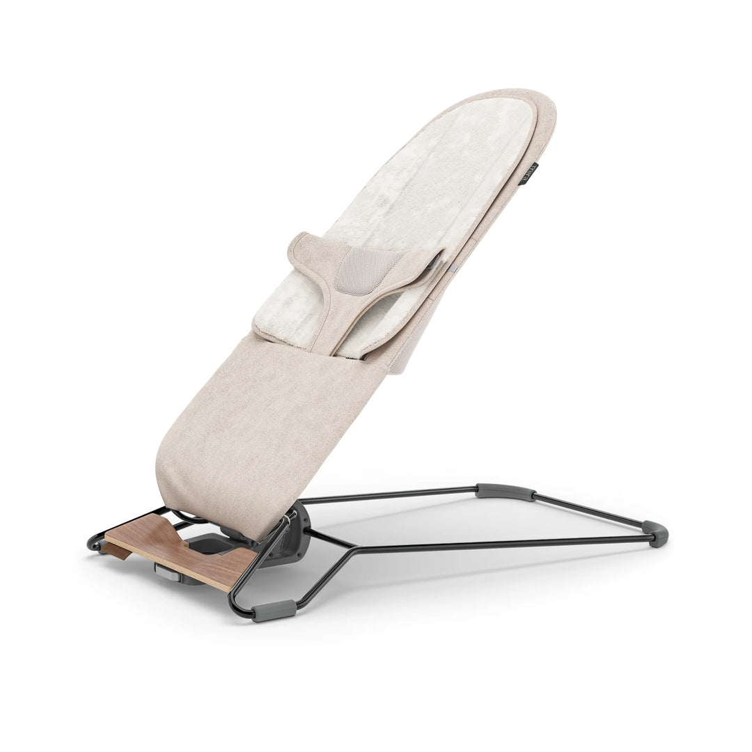 “UPPAbaby Mira Bouncer in Charlie beige fabric displayed in a reclined side view, featuring soft plush newborn insert, breathable mesh support, ergonomic design, and lightweight steel frame with wooden base accent.”