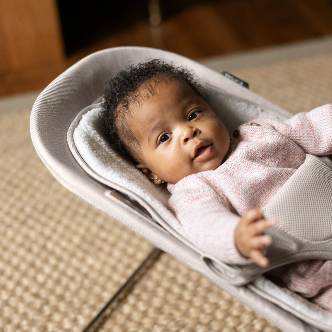 “Baby resting comfortably in the UPPAbaby Mira Bouncer in Charlie beige, featuring plush newborn insert and breathable mesh support, shown in a cozy home setting for lifestyle use.”