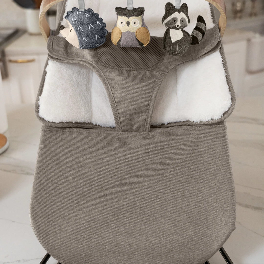“UPPAbaby Mira Bouncer in Wells taupe with plush newborn insert and wooden toy bar featuring soft animal toys—hedgehog, owl, and raccoon—shown in a modern kitchen setting for enhanced infant entertainment and comfort.”