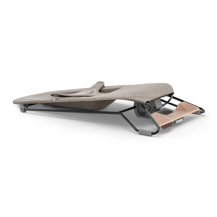 “UPPAbaby Mira Bouncer in Wells taupe folded flat for storage, showing ultra-slim collapsible design, breathable mesh seating, and lightweight steel frame with walnut-tone wood base for compact, modern baby gear.”