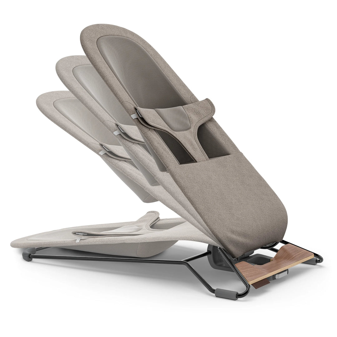 “UPPAbaby Mira Bouncer in Wells taupe demonstrating multiple recline positions, highlighting the adjustable ergonomic seat design, breathable mesh back panel, textured taupe upholstery, and lightweight steel frame with walnut-tone wood base.”