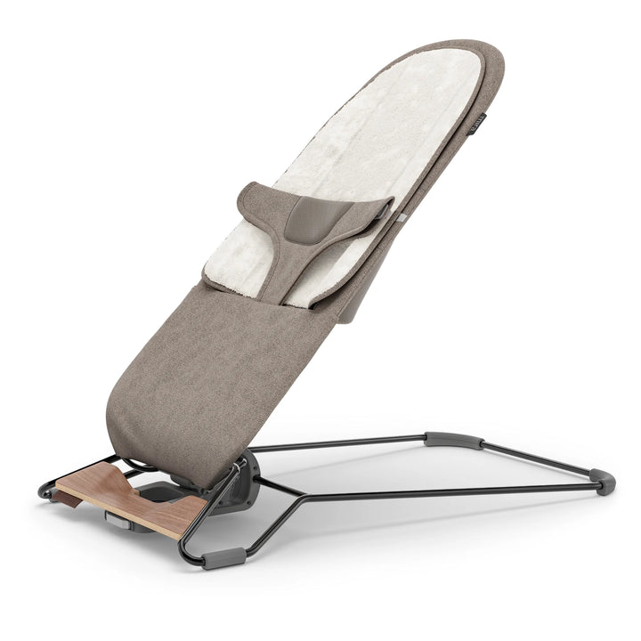 “UPPAbaby Mira Bouncer in Wells taupe shown in upright recline position, featuring soft newborn insert, breathable mesh back panel, ergonomic infant harness, and lightweight steel frame with walnut-tone wood base for modern nursery seating.”