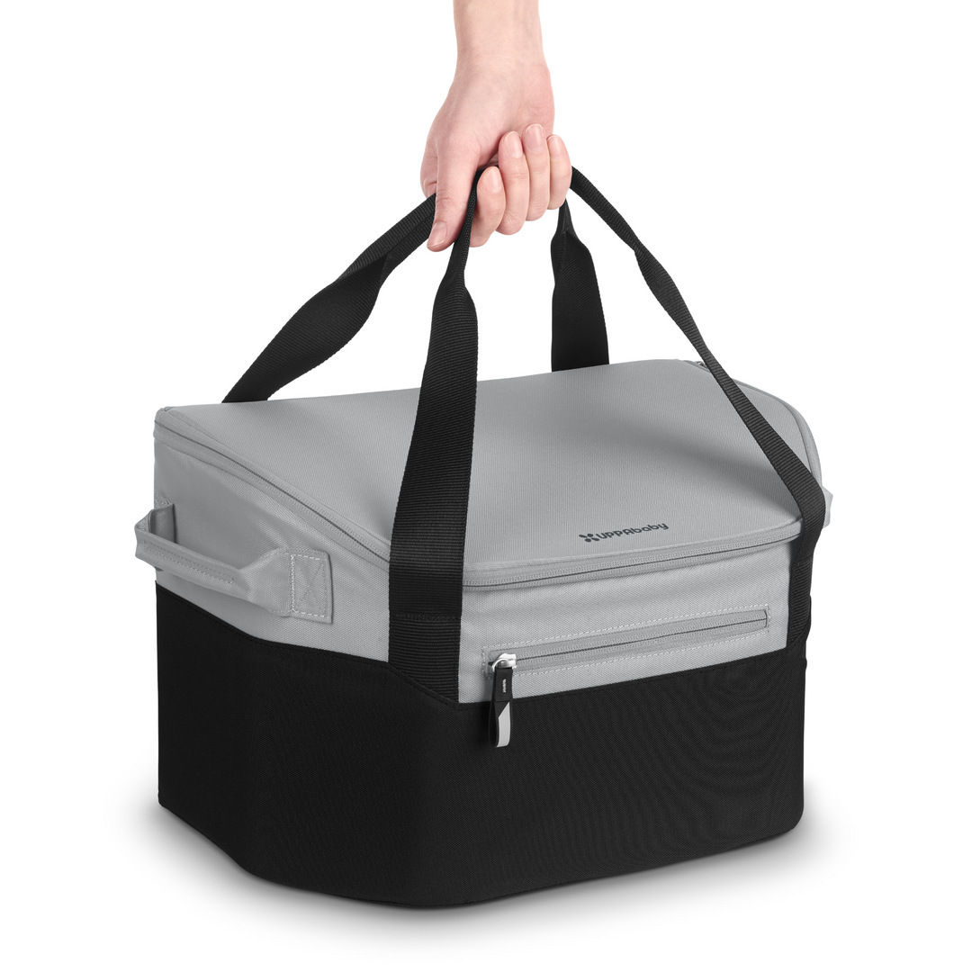 The UPPAbaby Bevvy stroller basket cooler product shot from the front. showing someone lifting it from the longer handles