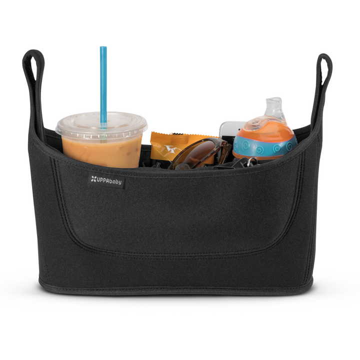 The UPPAbaby easy-clean stroller organiser is a must have for all parents. This image is a product shot of the organiser filled with essentials such as an iced coffee, flapjack snack, sunglasses, keys, phone and a toddlers juice bottle.