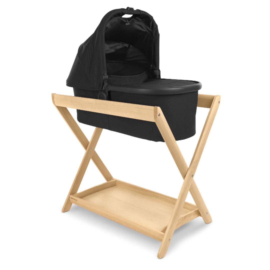 UPPAbaby Carrycot Stand in natural wood shown with the UPPAbaby Jake Carrycot attached, creating a secure elevated sleep solution with a modern minimalist design.