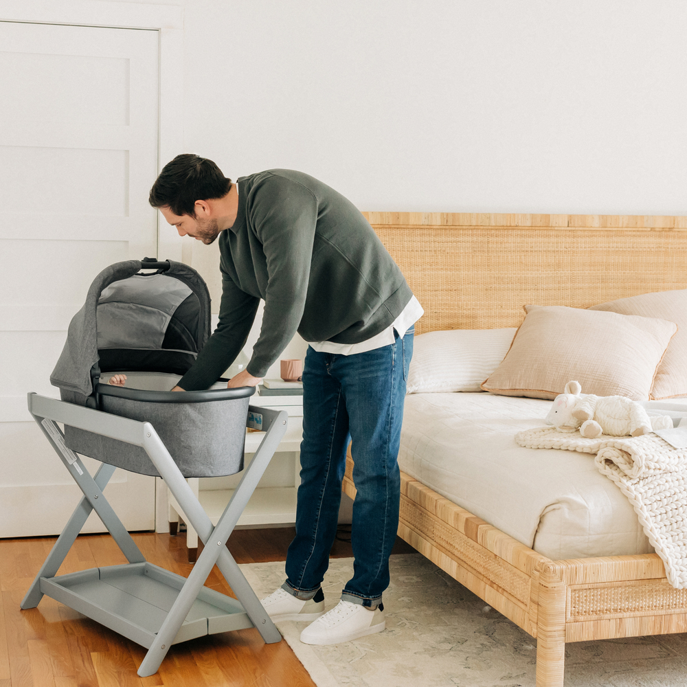 Father checking on his child that is lying in the carrycot attached to the carrycot stand next to the parents bed.
