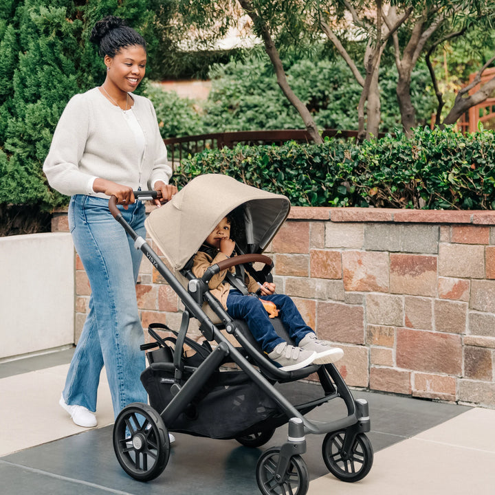 Parent pushing the UPPAbaby Vista V3 stroller in the Liam oatmeal colourway during an outdoor walk, showing the extended canopy, toddler seated comfortably, all-terrain wheels and spacious under-seat storage basket.