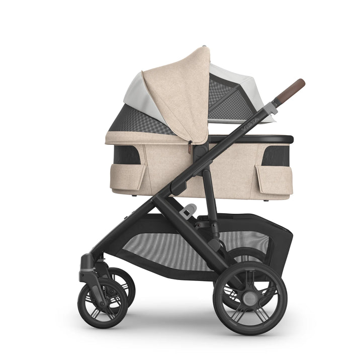 Side view of the UPPAbaby Vista V3 carrycot in the Liam oatmeal colourway attached to the stroller chassis, showing the ventilated canopy with open airflow panels, padded bassinet design, leather-accented handlebar and large under-seat storage basket.