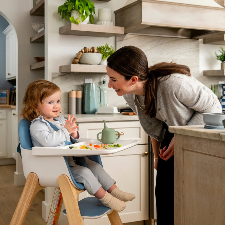 Woman interacting with a child in a high chair in a kitchen.