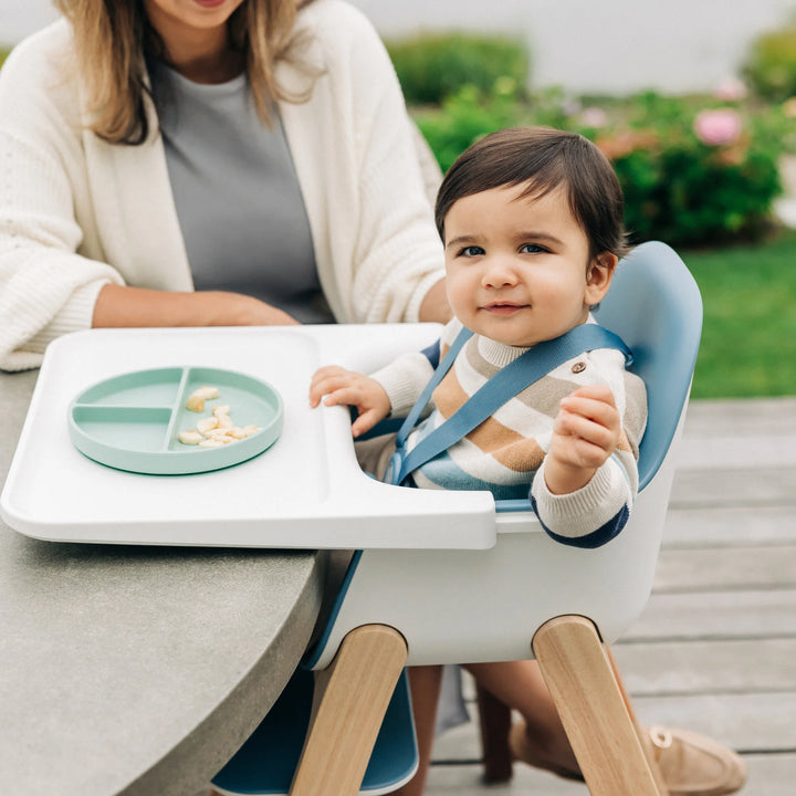 Child in a high chair with a tray and plate outdoors