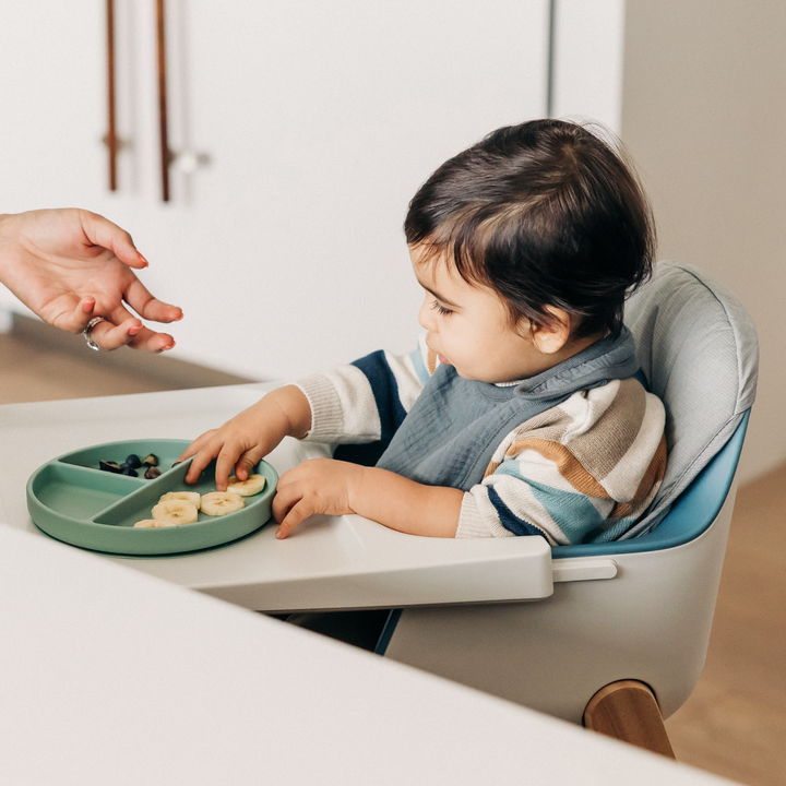 This image shows a toddler eating a banana snack on his high chair with the high chair cushion