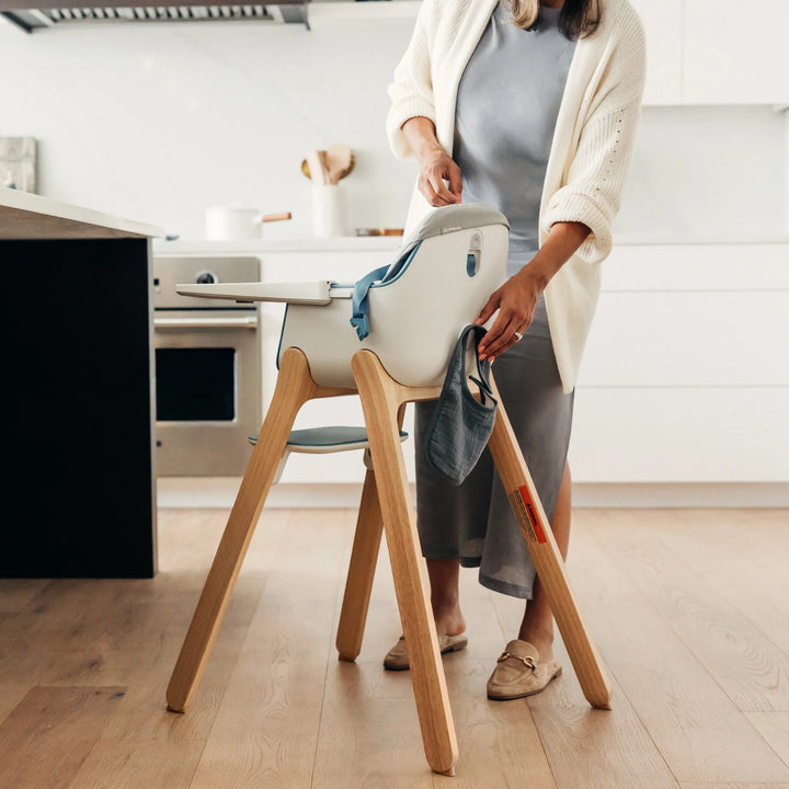 Lifestyle image of an adult cleaning the floor around the UPPAbaby Ciro high chair with grey cushion accessory, highlighting its lightweight design and easy-to-clean wooden legs