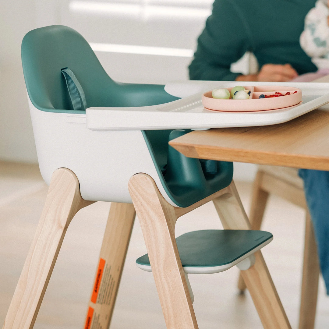 Children's high chair with wooden legs and green seat at a dining table.