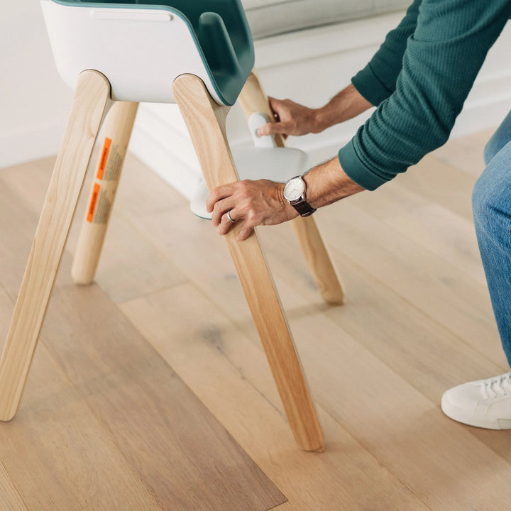 Person easily adjusting the UPPAbaby high chair with wooden legs.