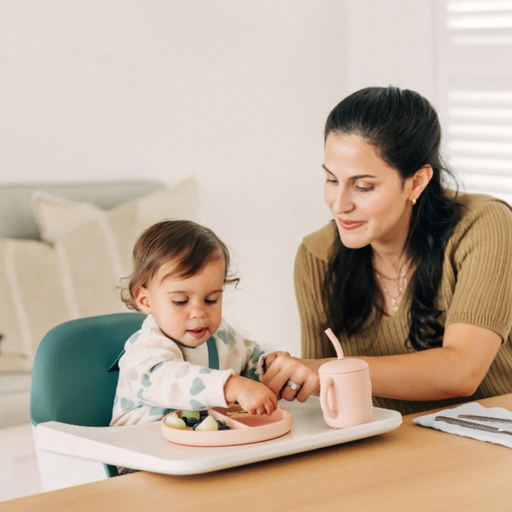 Toddler eating at the table in an UPPAbaby Ciro High Chair Emrick while mom assists, showcasing modern ergonomic high chair design for safe, comfortable mealtime.
