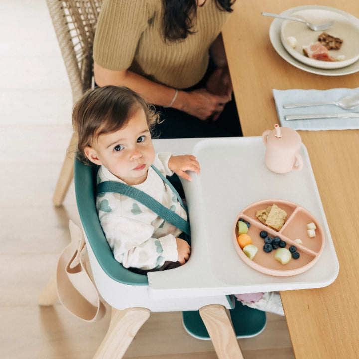 Toddler sitting in UPPAbaby Ciro High Chair Emrick at the table eating a healthy snack, showcasing ergonomic modern high chair design for safe and comfortable mealtime.