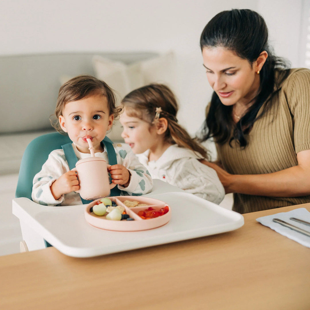 Woman and two children at a dining table with a high chair, food, and drinks.