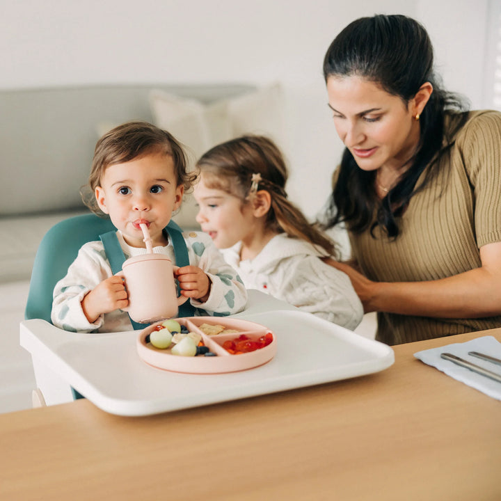 Woman and two children at a dining table with a high chair, food, and drinks.