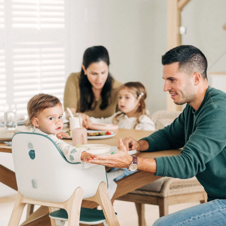 Toddler sitting in UPPAbaby Ciro High Chair Emrick at the family dining table with parents and sibling, showcasing modern ergonomic high chair design for safe mealtime and family bonding.