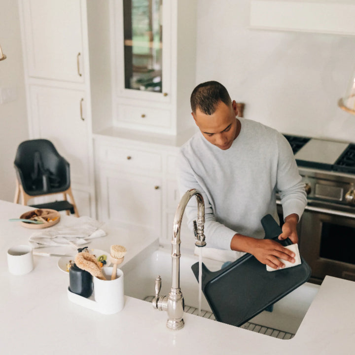 Dad cleaning UPPAbaby Ciro High Chair Jake tray in modern kitchen, demonstrating easy-to-clean, removable high chair tray for hassle-free baby mealtime cleanup.