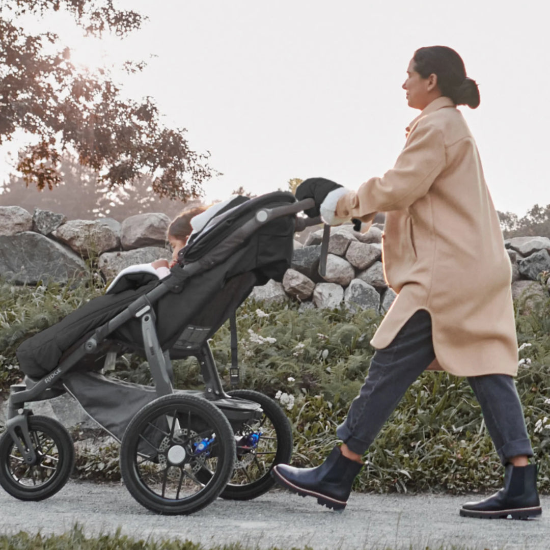 UPPAbaby Cozy Handmuffs Jake black stroller hand warmers in use on an UPPAbaby pushchair, keeping parents’ hands warm during outdoor walks in cold weather.