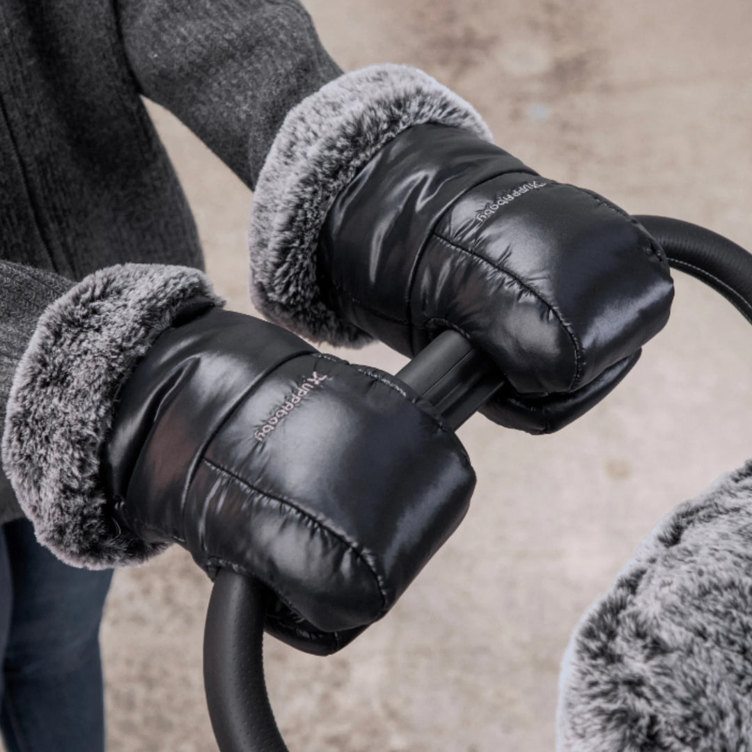 UPPAbaby Cozy Handmuffs Luxe attached to stroller handlebar, black premium pram hand warmers with plush faux-fur lining keeping hands warm in cold weather.