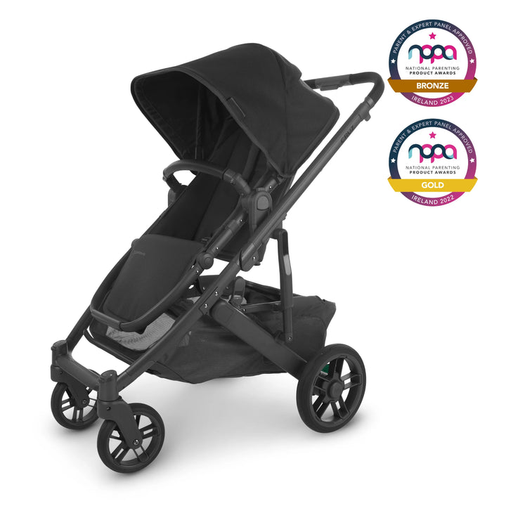 The UPPAbaby Cruz V2 in Jake is an all black stroller with a charcoal fabric, carbon frame and black REACH certified leather accents. The stroller is angled to the left and the NPPA awards logos are visible in the top right of the image