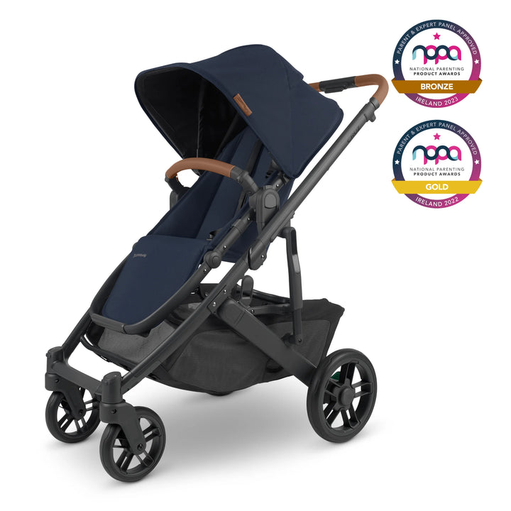 The UPPAbaby Cruz V2 in Noa has a navy fabric, carbon frame and saddle REACH certified leather accents. The stroller is angled to the left and two NPPA awards logos are visible on the top right of the image