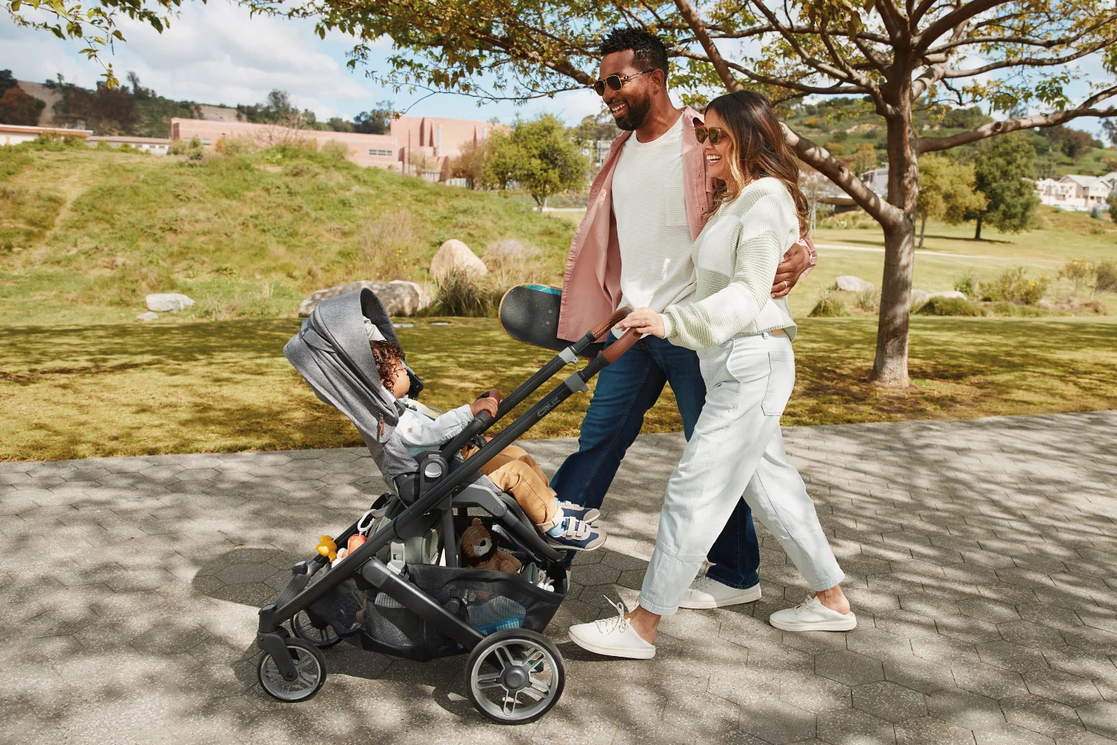 Parents smiling and walking in the park with their toddler in the UPPAbaby Cruz V3 pushchair.