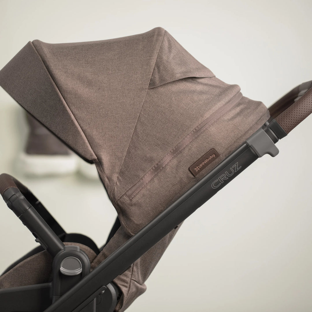 Close up of the mocha melange fabric and 'Cruz' lazer etched logo on the Cruz V3 stroller.