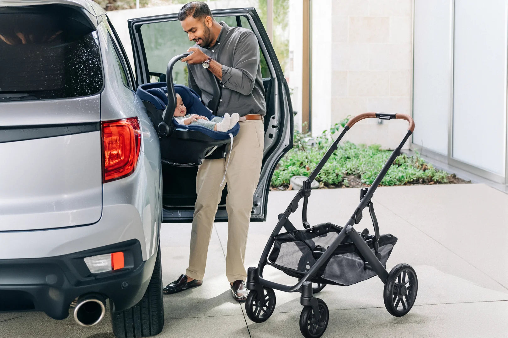 This image depicts a father taking the Mesa i-Size car seat off of the Vista chassis and placing it in the back seat of their car.