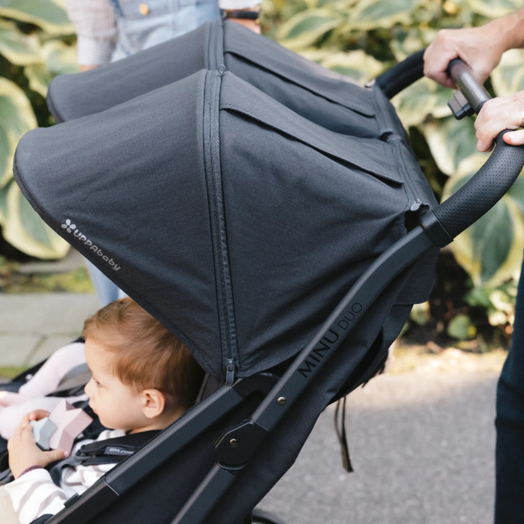 Close-up of UPPAbaby Minu Duo Jake black double stroller canopy, showing large sunshade and compact frame while being pushed outdoors