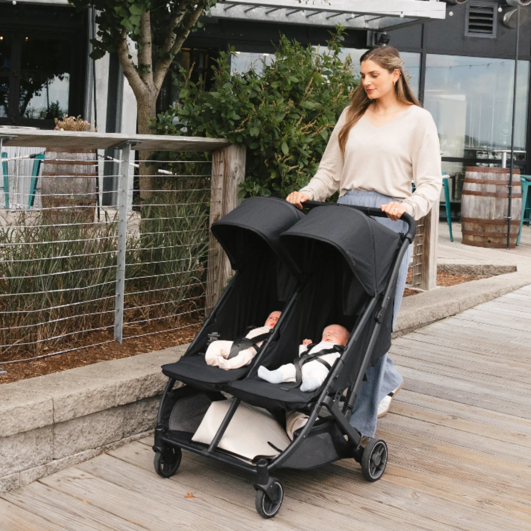 Woman pushing UPPAbaby Minu Duo double stroller in Jake black with two babies, compact twin/sibling pushchair outdoors