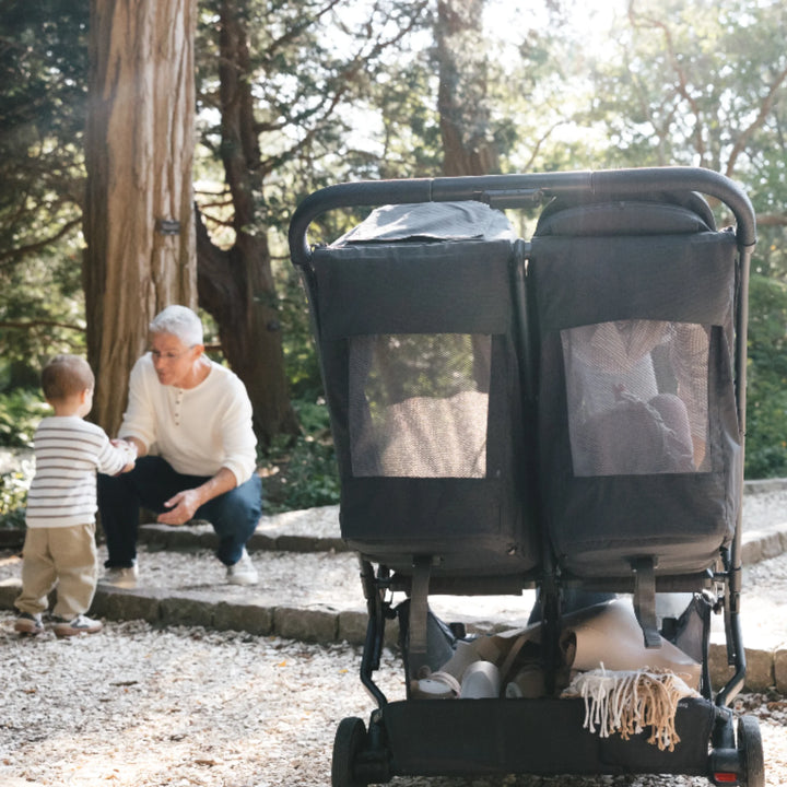 Rear view of UPPAbaby Minu Duo Jake black double stroller showing mesh ventilation panels and recline seats, used outdoors in a park