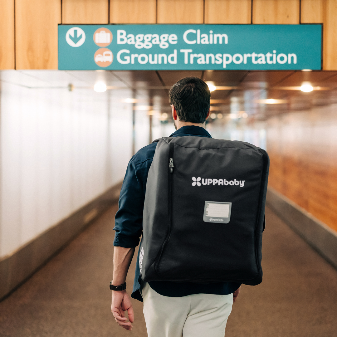 This image is of a parent walking towads the baggage claim and ground transportation area of an airport with the Minu V2 travel bag on their back