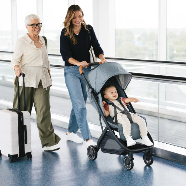 UPPAbaby MINU V3 Dillan lightweight travel stroller at airport, parent pushing toddler while travelling with suitcase”