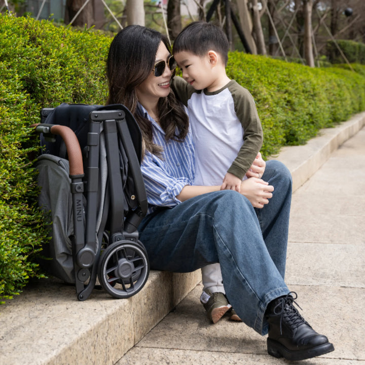 “Woman sitting on a low step with a child beside a folded UPPAbaby MINU V3 stroller in Greyson,